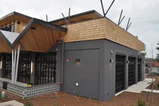 Thumbnail for Modern commercial building with dark gray brick walls, wood shingles, large windows, and unique angled roof design.
