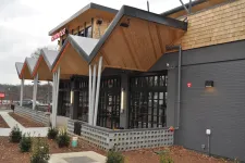 Thumbnail for Modern commercial building with angular wooden eaves, gray brick walls, and large window panels under an overcast sky