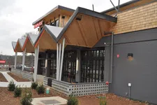 Thumbnail for Modern restaurant exterior with zigzag wooden roof, large windows, and landscaped walkway under cloudy sky