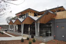 Thumbnail for Modern restaurant exterior with geometric roof design, wooden accents, large windows, and landscaped surroundings.