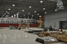 Thumbnail for Interior of a large warehouse under construction with equipment, pallets, and workers on scissor lifts.