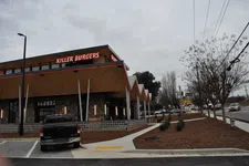 Thumbnail for Modern Killer Burgers restaurant with distinctive peaked roof and cloudy sky, parked truck, and street view.