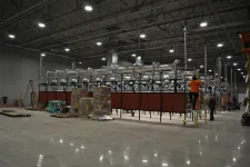 Thumbnail for Large industrial warehouse with ventilation system, packed boxes, and workers installing equipment on a ladder.