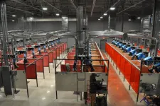 Thumbnail for Industrial workshop with rows of welding stations separated by red and orange safety curtains under bright overhead lights.