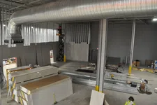 Thumbnail for Interior view of a warehouse under construction with drywall stacks, steel beams, and a worker in safety gear.