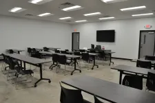Thumbnail for Modern empty classroom with black chairs, gray tables, concrete floor, and a large monitor on white wall.