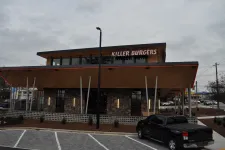 Thumbnail for Modern Killer Burgers restaurant building with wood and stone facade and parked black pickup truck under overcast sky