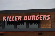 Thumbnail for Neon pink sign reading Killer Burgers mounted on modern wooden and black storefront under cloudy sky.