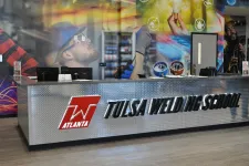 Thumbnail for Reception desk with Tulsa Welding School logo inside a modern building with industrial-themed wall art.