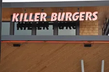 Thumbnail for Killer Burgers restaurant sign with bold pink letters on wood panel exterior under an overhang.