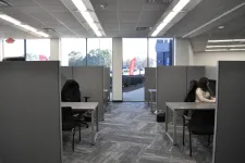 Thumbnail for Office cubicles with gray partitions and desks, a woman working on a computer by the window, bright natural light.