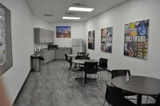 Thumbnail for Corporate break room with round tables, black chairs, kitchenette, refrigerator, and motivational posters on walls.