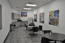 Thumbnail for Modern office break room with kitchen area, round tables, black chairs, motivational posters, and a gray floor.