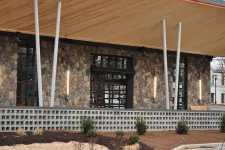 Thumbnail for Modern building exterior with stone wall, large windows, vertical lights, and wooden roof overhang.