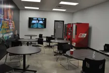 Thumbnail for Modern break room with round tables, black chairs, vending machines, TV screen, and motivational wall graphics.