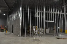 Thumbnail for Construction site interior with metal stud framing for walls, stacks of drywall, and a worker in safety vest.