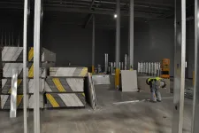 Thumbnail for Worker installing drywall panels inside a large, unfinished warehouse with metal framing and construction materials.