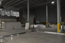 Thumbnail for Large warehouse interior under construction with drywall sheets, metal beams, and construction tools scattered.