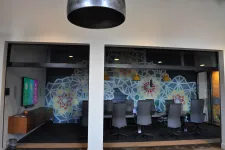 Thumbnail for Modern conference room with colorful geometric wall art, black chairs, wooden table, and hanging pendant lights.