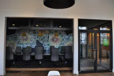 Thumbnail for Modern office conference room with black chairs, geometric wall art, and glass entrance doors under hanging lights