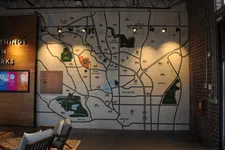 Thumbnail for Large wall map of city neighborhoods and parks displayed in a modern indoor space with chairs and wooden decor.