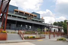 Thumbnail for Modern restaurant building with outdoor seating, stairs, ramps, and flower beds under partly cloudy sky.
