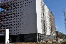 Thumbnail for Modern building with perforated geometric facade panels and leafless trees under clear blue sky.