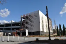 Thumbnail for Modern multi-level parking garage with geometric facade under clear blue sky with scattered clouds.