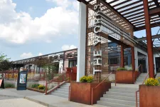 Thumbnail for Exterior of a modern building with rust-colored metal structure and stairs under a cloudy sky.