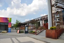 Thumbnail for Outdoor urban plaza with colorful mural, modern buildings, stairway, and clear sky with scattered clouds.