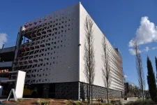 Thumbnail for Modern multi-story parking garage with perforated metal facade and tall trees under clear blue sky