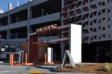 Thumbnail for Entrance to a multi-level parking garage with orange and white signage and barriers under daylight.