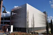 Thumbnail for Modern parking garage with perforated metal facade and trees under blue sky with scattered clouds.