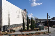 Thumbnail for Modern building with perforated white facade, tall trees, pathways, and clear blue sky in an urban landscape.