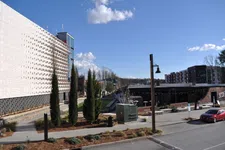 Thumbnail for Modern urban street scene with trees, contemporary buildings, clear sky, and parked red car on a sunny day.