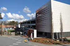 Thumbnail for Modern multi-level parking garage next to a fenced green space park under a blue sky with clouds.