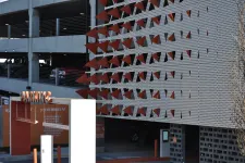 Thumbnail for Modern parking garage entrance with orange triangular accents and visible parked cars inside the structure
