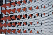 Thumbnail for Facade with rows of red triangular metal elements mounted on perforated white panels of a building exterior.