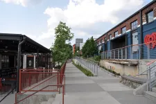 Thumbnail for Outdoor urban walkway with red railings, trees, and modern buildings on a partly cloudy day.
