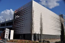 Thumbnail for Modern parking garage exterior with geometric perforated panels and tall thin trees under a blue sky.