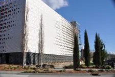 Thumbnail for Modern building with perforated white facade and black base surrounded by tall trees on a sunny day.
