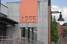 Thumbnail for Modern building facade with large orange address number 1255 on gray concrete wall near a staircase and street lamp.