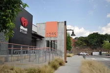 Thumbnail for Modern iHeart Media building entrance with ramp, concrete and glass facade, and clear blue sky above.
