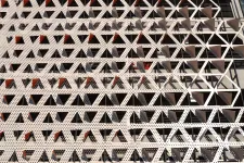 Thumbnail for Facade of a modern building with repeating perforated white triangular patterns creating geometric shadows.