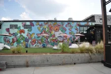 Thumbnail for Outdoor seating area with umbrellas in front of a colorful butterfly mural on a building wall.