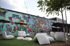 Thumbnail for Outdoor seating area with modern white chairs and colorful butterfly mural on building wall under string lights.