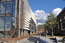 Thumbnail for Modern urban street with contemporary buildings, trees, benches, and a clear sky with clouds.