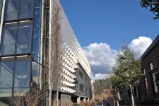Thumbnail for Modern building with glass panels and geometric facade under a blue sky with clouds and surrounding trees.