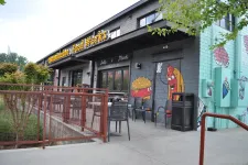 Thumbnail for Exterior of a restaurant with murals of a cheeseburger and hot dog waving, outdoor seating, and a red metal fence.