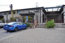 Thumbnail for Blue sedan parked in front of a gray industrial Makers Building with stairs and greenery on a cloudy day
